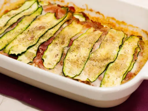 Sformato di zucchine appena sfornato, con fette sottili di zucchina grigliata, prosciutto e formaggio filante, condito con pepe nero.