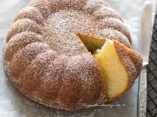 Torta 7 vasetti soffice e dorata, spolverata di zucchero a velo. Una fetta è stata tagliata, rivelando l'interno profumato.