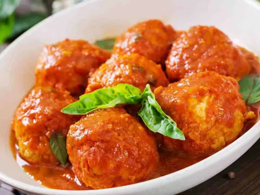 Polpette al sugo succulente in un piatto bianco, guarnite con foglie di basilico fresco. Un classico della cucina italiana.