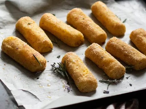 Crocchette di patate al forno dorate e croccanti, adagiate su carta forno con rametti di rosmarino e fiori di lavanda.