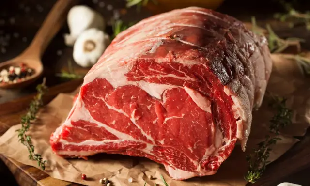 Un succulento pezzo di carne cruda, pronto per diventare un delizioso brasato di manzo. Spezie, erbe aromatiche e aglio completano la scena.