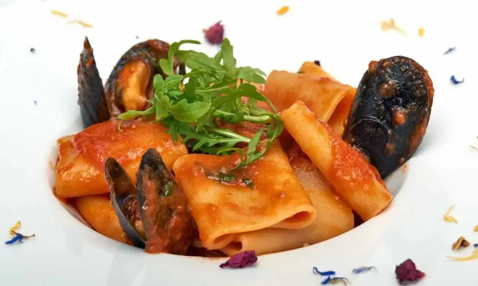 Paccheri allo scoglio con cozze e pomodoro, guarniti con rucola fresca e petali di fiori.