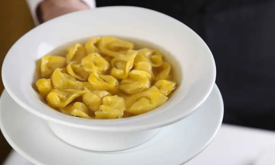 Un piatto fumante di tortellini in brodo, un classico comfort food italiano, servito in una ciotola bianca.