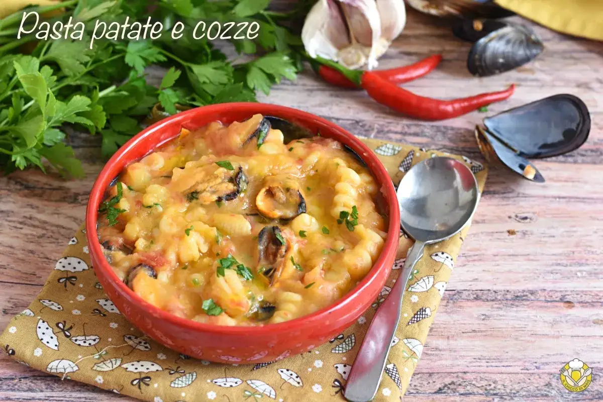 Un invitante piatto di pasta patate e cozze, guarnito con prezzemolo fresco, su un tovagliolo decorato. Sullo sfondo, aglio, peperoncini e cozze.