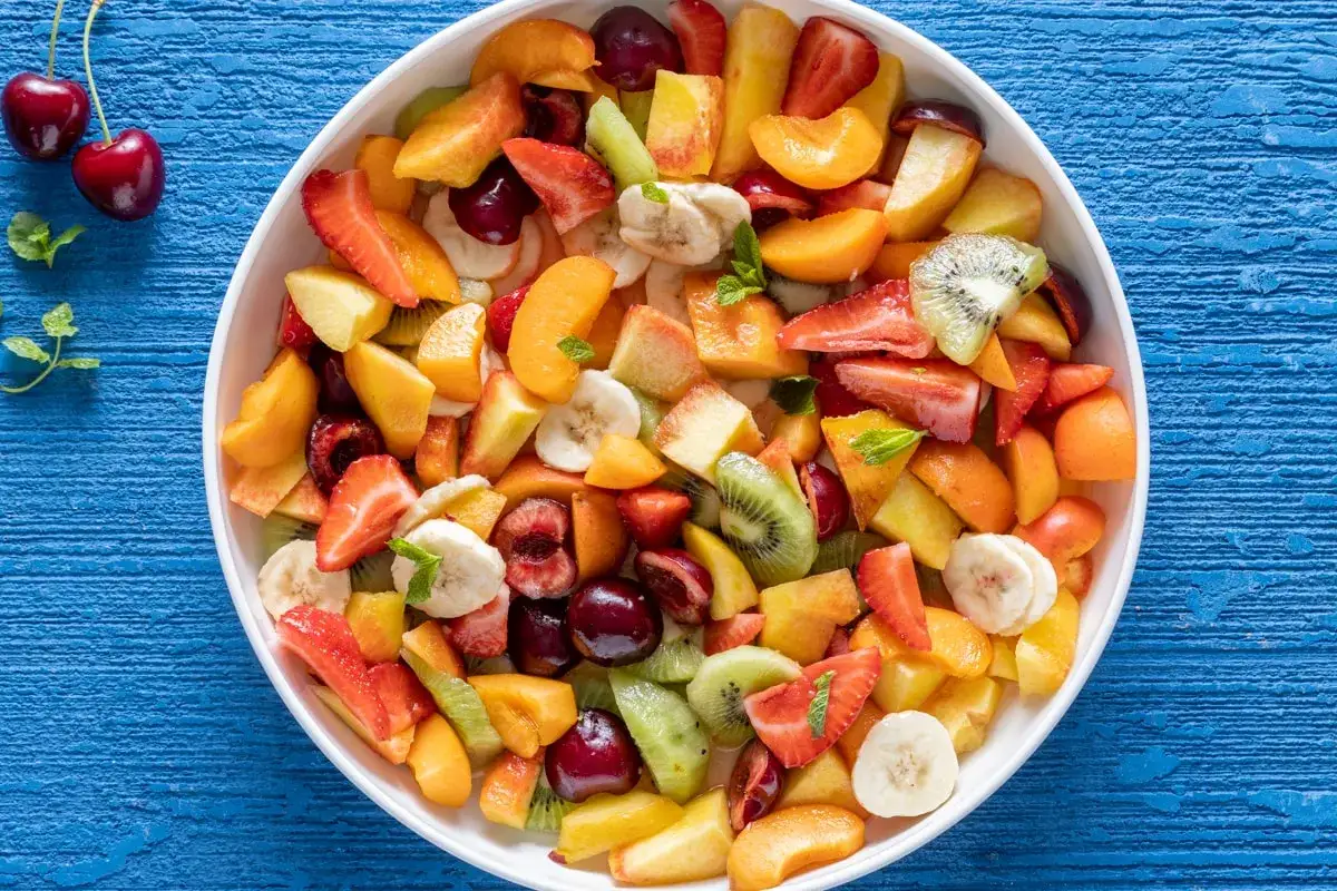 Una colorata macedonia di frutta, con fragole, kiwi, pesche, banane e ciliegie, pronta per essere gustata.
