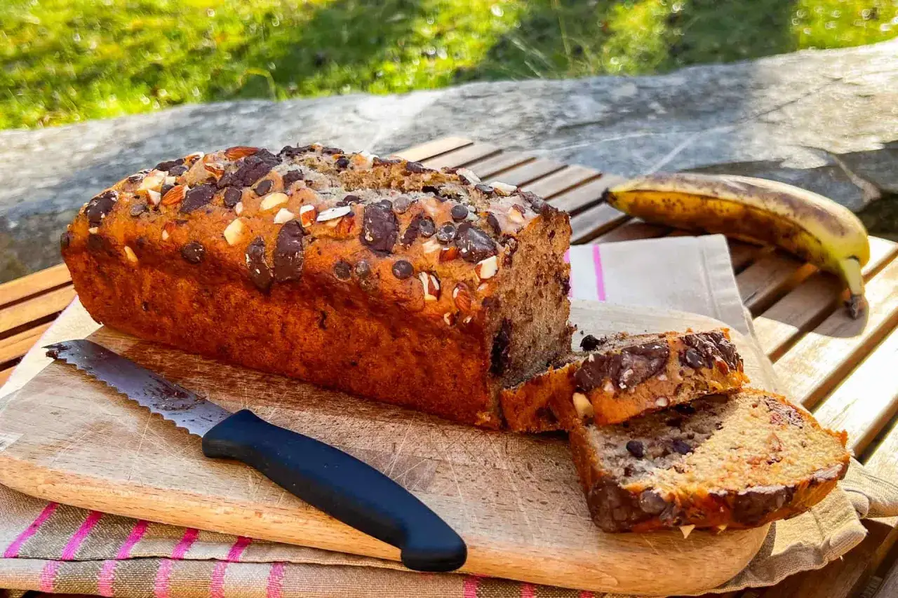 Delizioso banana bread vegano con gocce di cioccolato e mandorle, pronto per essere gustato all'aperto.