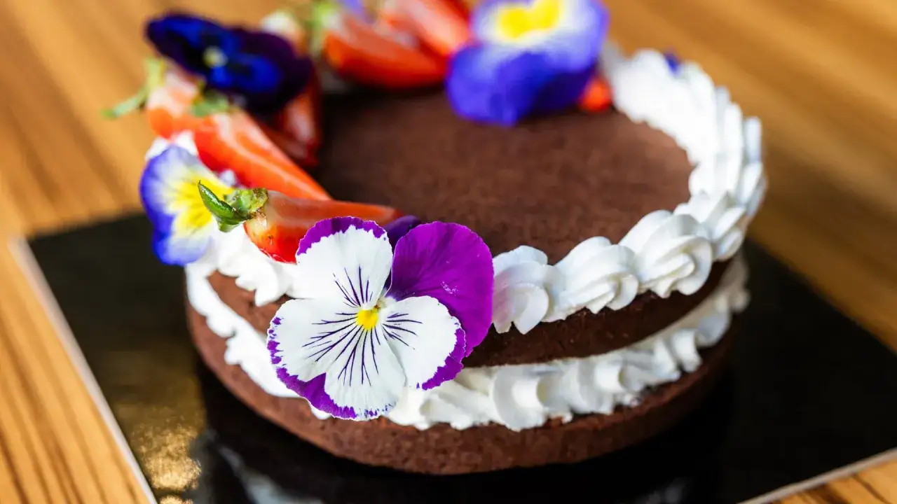 Deliziosa torta festa della mamma al cioccolato, decorata con panna montata, fragole e fiori colorati.