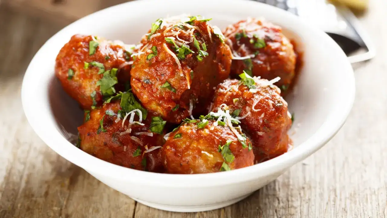 Polpette di carne succulente in salsa rossa, guarnite con parmigiano grattugiato e prezzemolo fresco. Un piatto invitante.