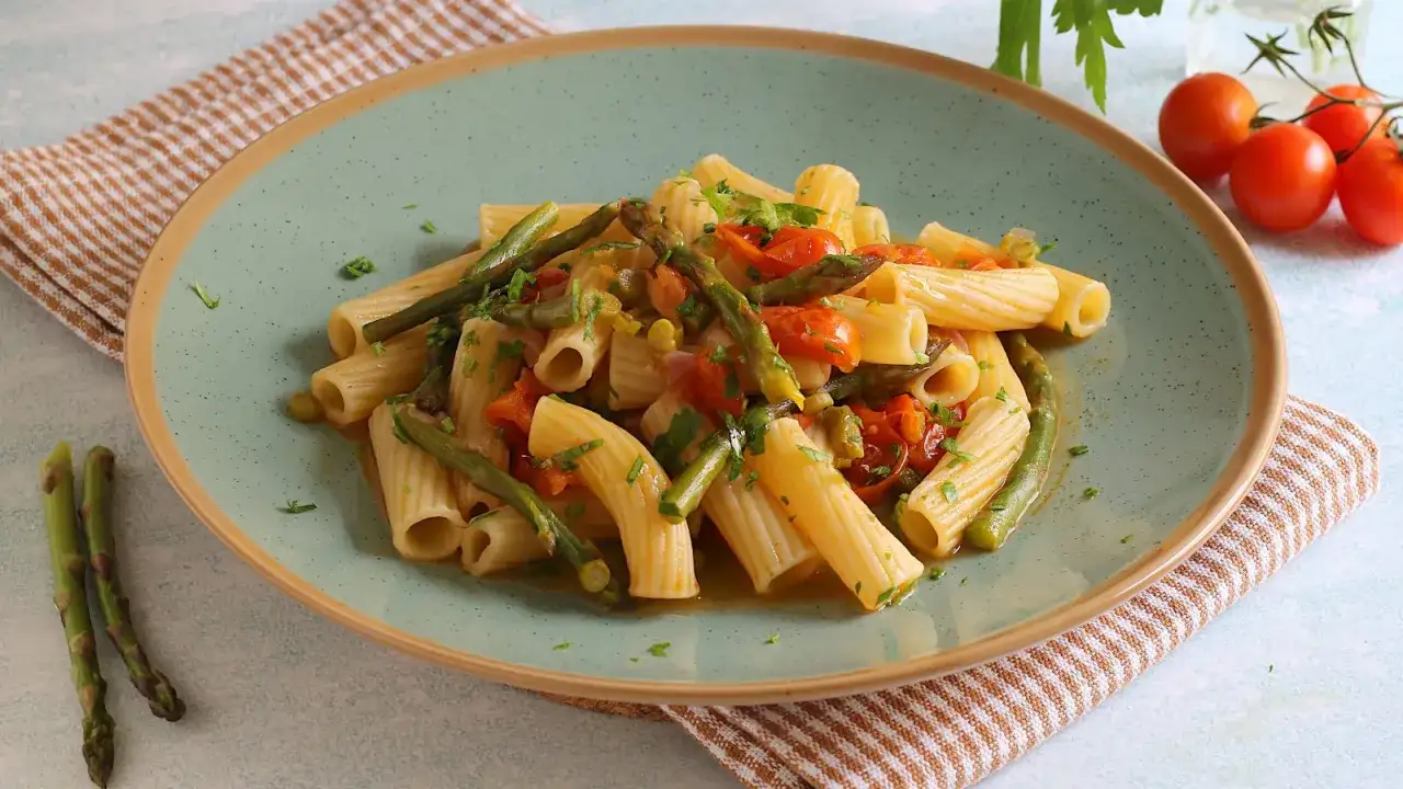 Piatto di pasta con asparagi e pomodorini, un classico della cucina italiana, condito con erbe fresche.