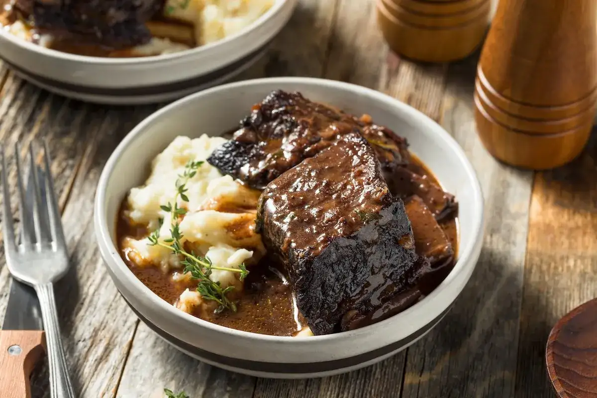 Un invitante brasato di manzo succulento servito con purè di patate cremoso e guarnito con timo fresco.