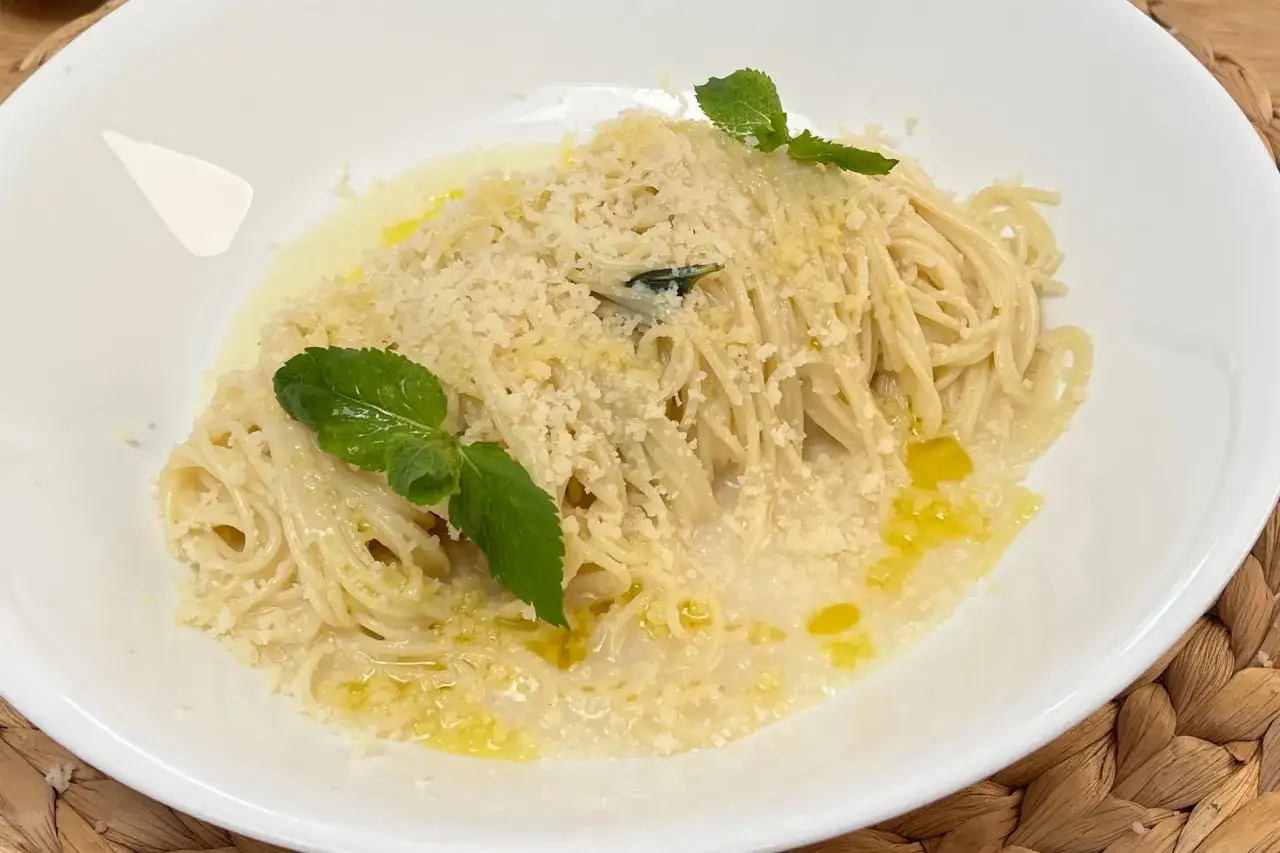 Spaghetti al limone cremosi, conditi con parmigiano e guarniti con foglie di menta fresca.