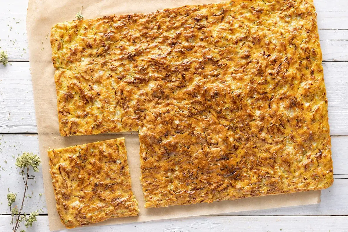 Schiacciata di zucchine dorata e croccante, tagliata a fette quadrate, su carta da forno.
