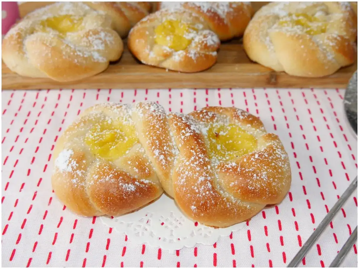 Dolci lievitati con crema gialla, spolverati di zucchero a velo come un fiocco di neve.