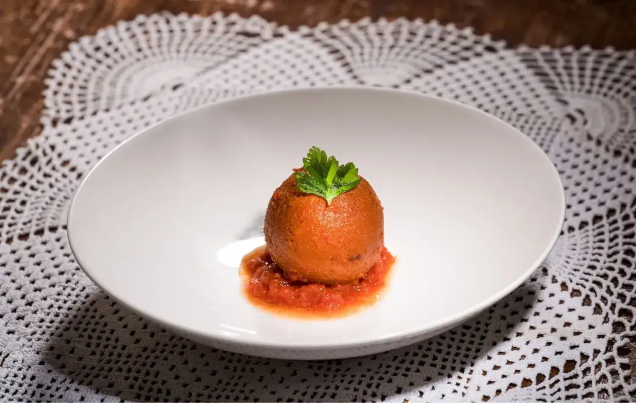 Una pallotta cacio e ova, dorata e gustosa, adagiata su un letto di salsa di pomodoro e guarnita con prezzemolo fresco.