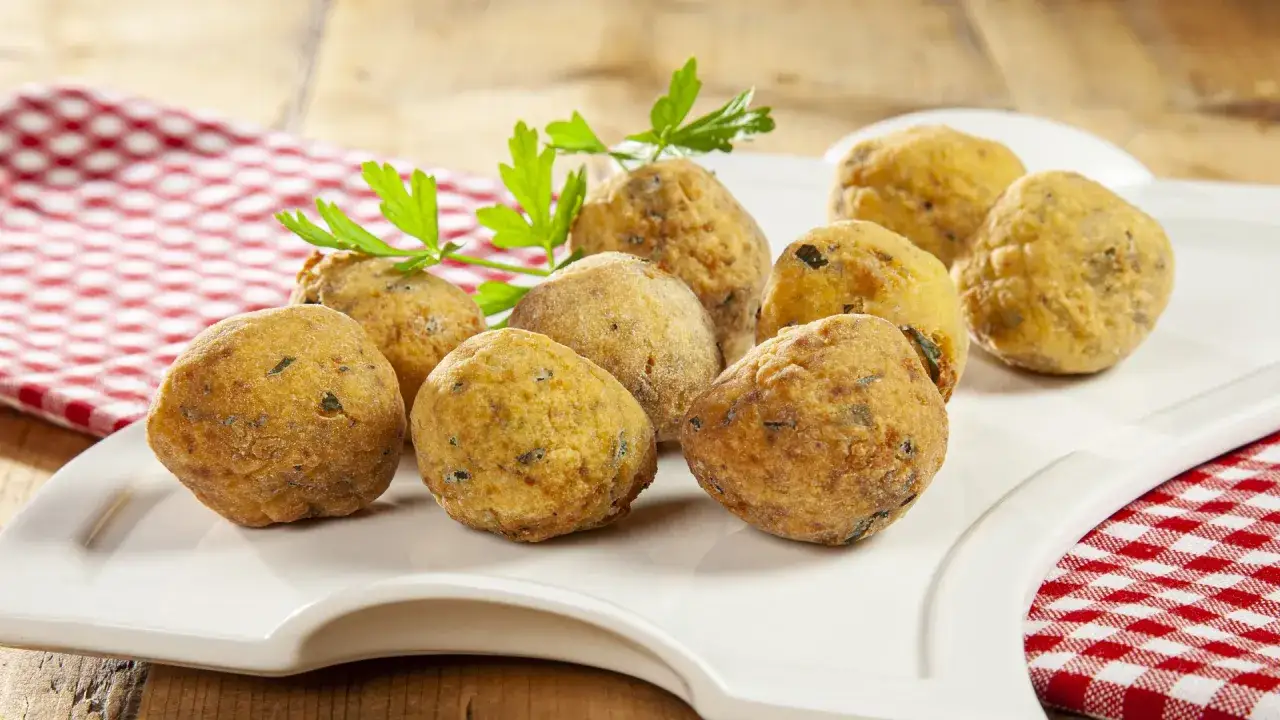 Polpette di pane dorate e croccanti, guarnite con prezzemolo fresco, su un piatto bianco con tovaglietta a quadri rossi.