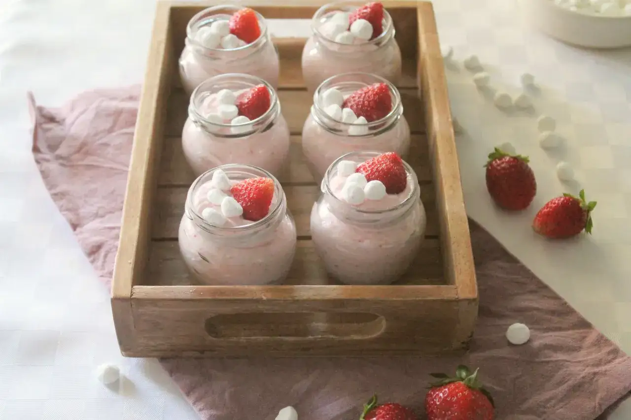 Sei vasetti di deliziosa mousse di fragole, guarniti con fragole fresche e soffici marshmallow, pronti per essere gustati.