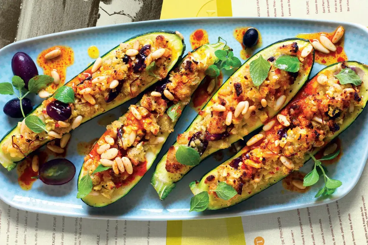Zucchine ripiene vegetariane con pinoli, olive e erbe aromatiche, servite su un piatto azzurro.