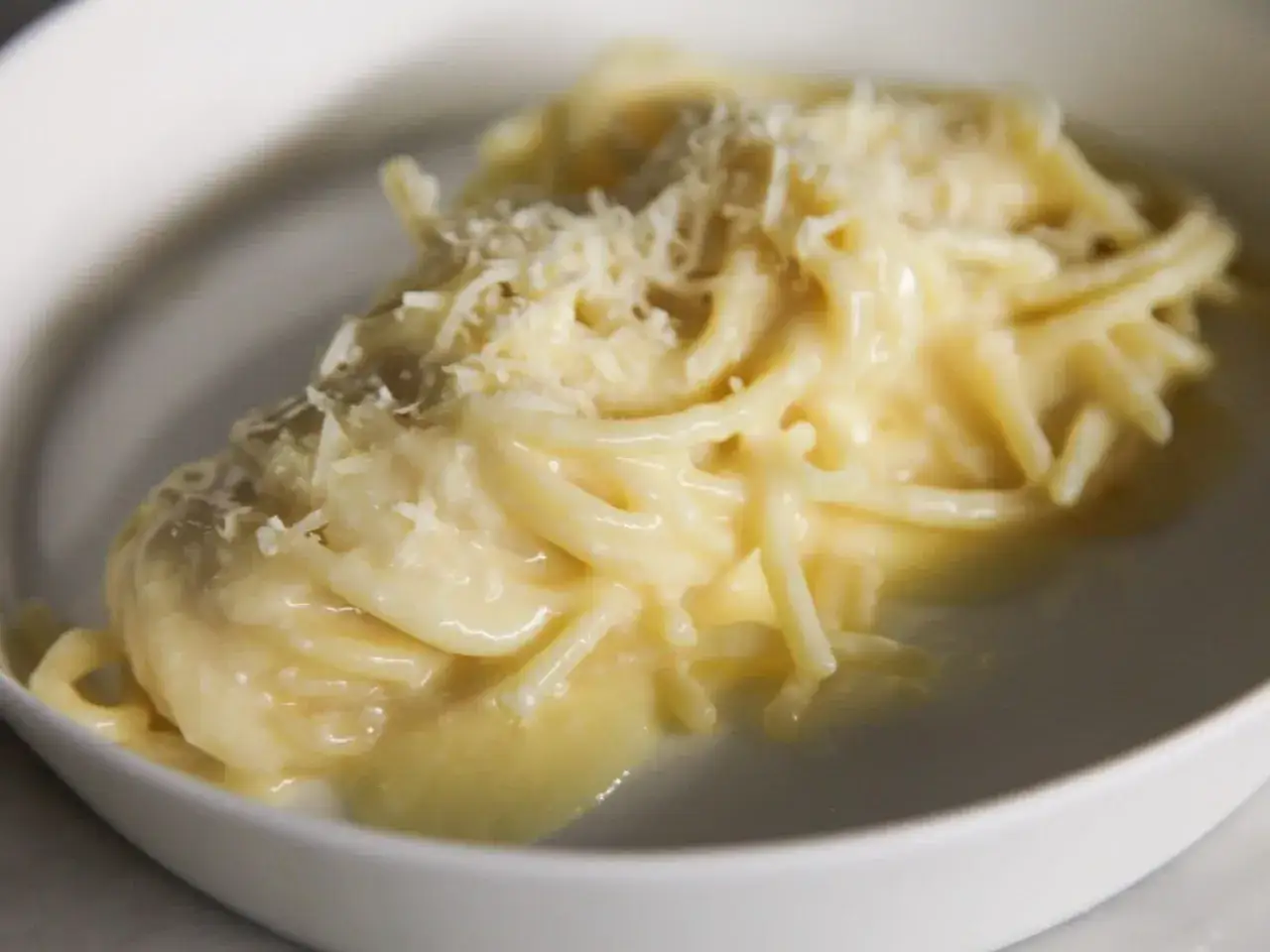 Un piatto di pasta in bianco cremosa, condita con abbondante parmigiano grattugiato.