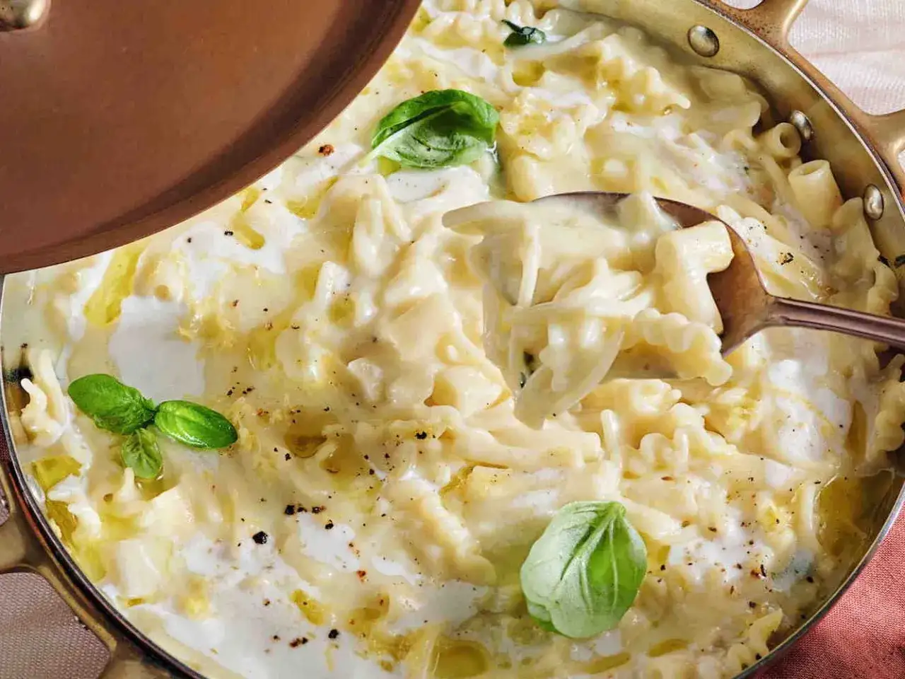 Un cucchiaio solleva una porzione cremosa di pasta patate e provola, guarnita con basilico fresco.