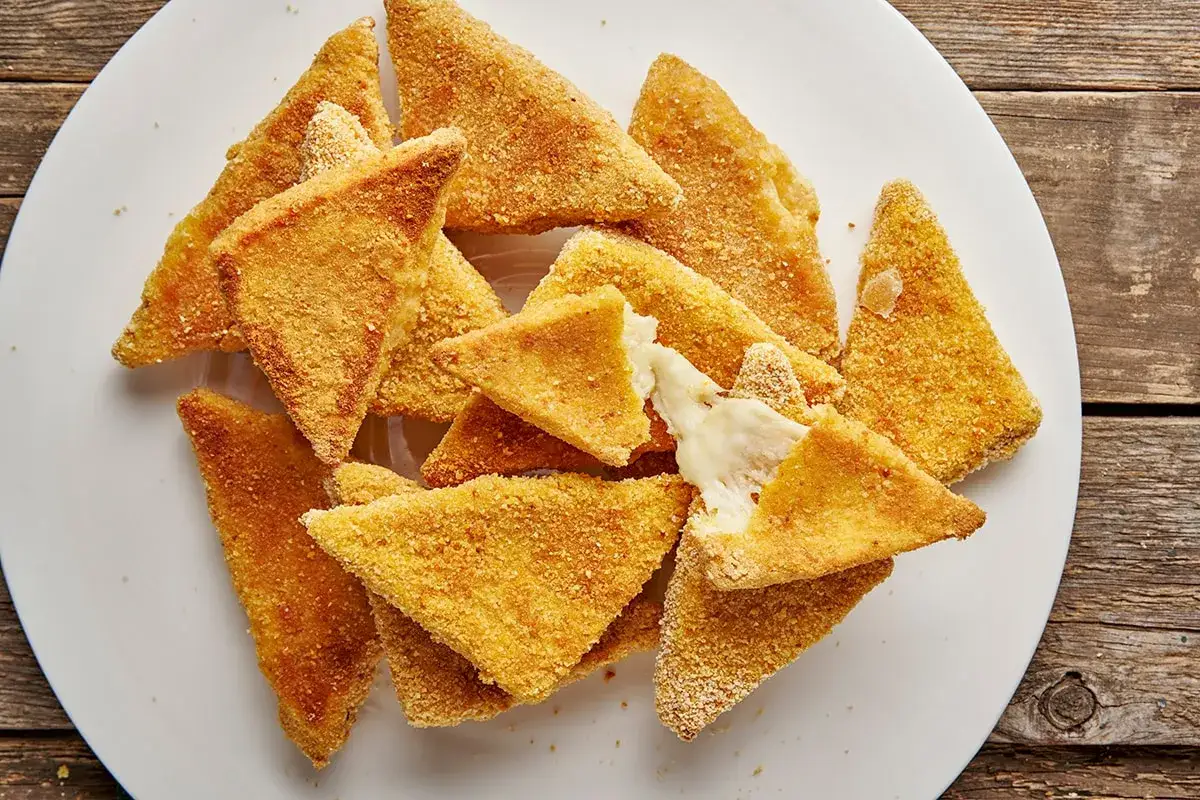 Mozzarella in carrozza al forno, triangolini dorati e croccanti con cuore filante di formaggio fuso, serviti su un piatto bianco.