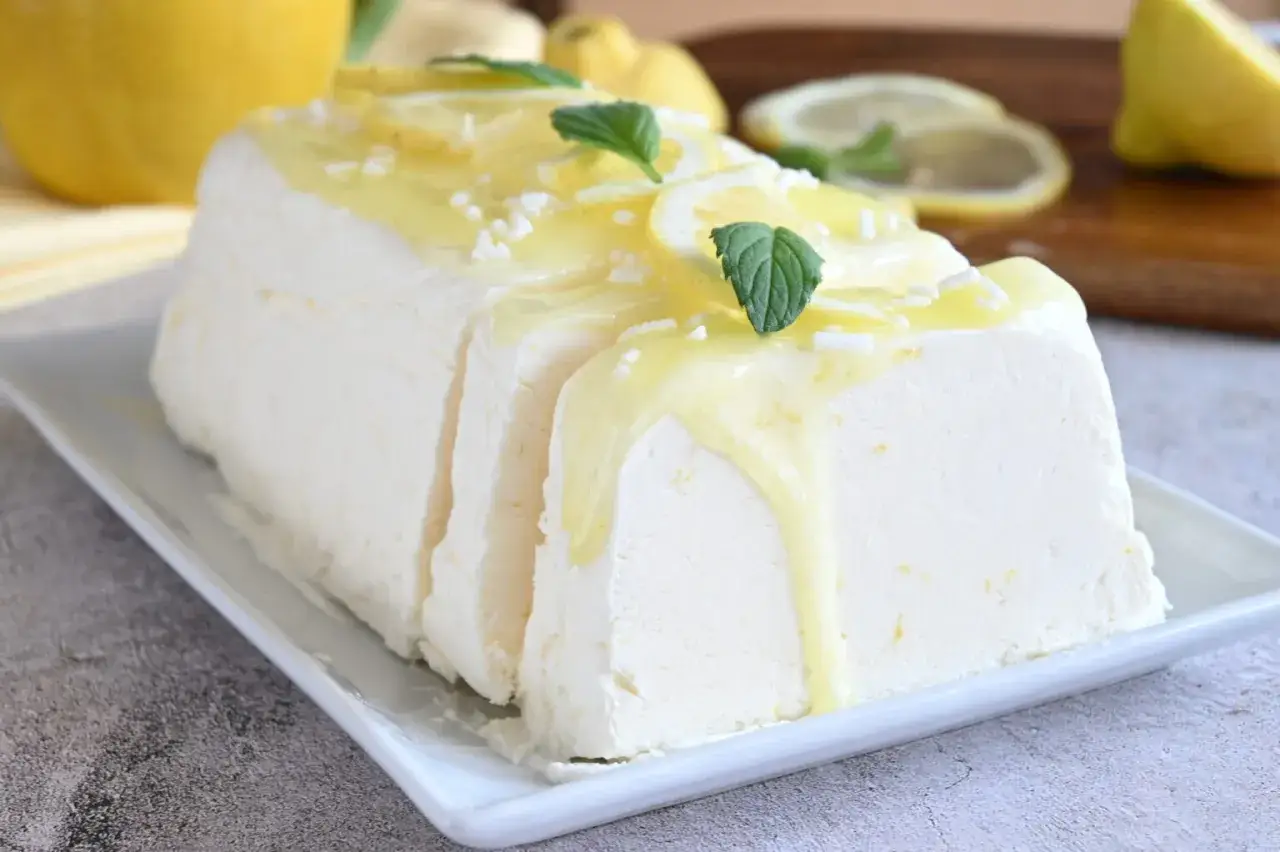 Un delizioso semifreddo al limone, guarnito con scorzette, menta e una glassa gialla brillante. Perfetto per un dessert rinfrescante.