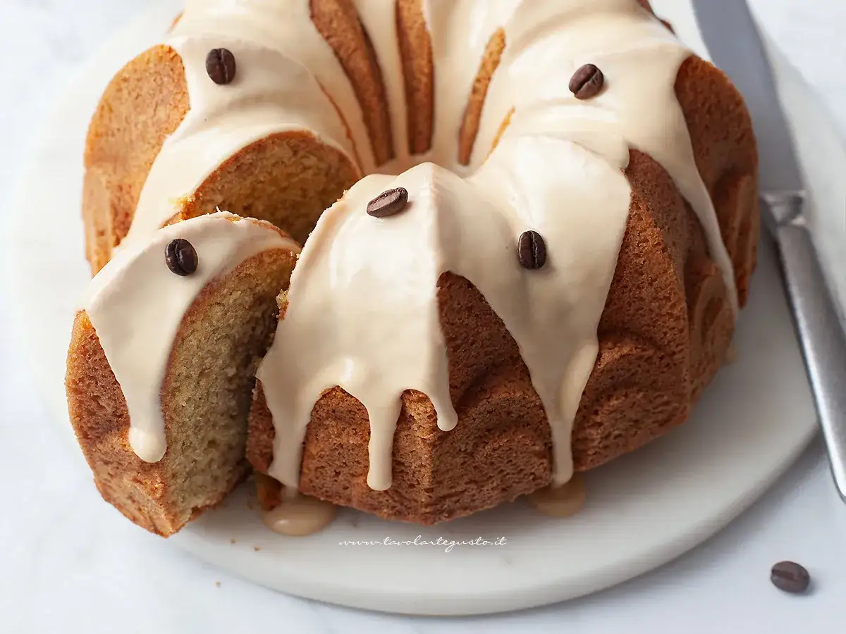 Deliziosa torta al caffè con glassa chiara e chicchi di caffè come decorazione. Una fetta è stata tagliata, rivelando l'interno soffice.