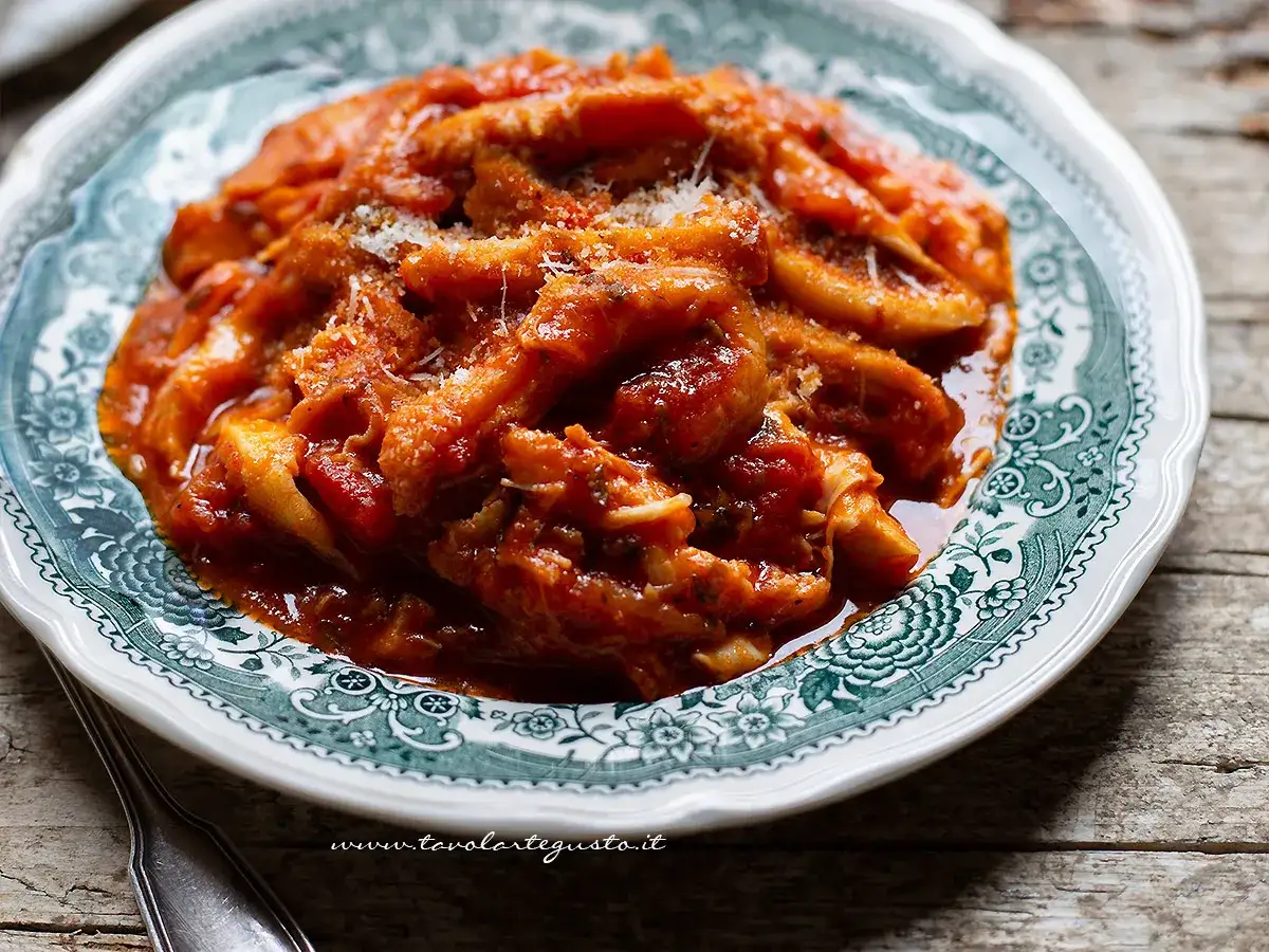 Un piatto di trippa alla romana fumante, condita con sugo rosso e formaggio grattugiato, servita su un piatto decorato.