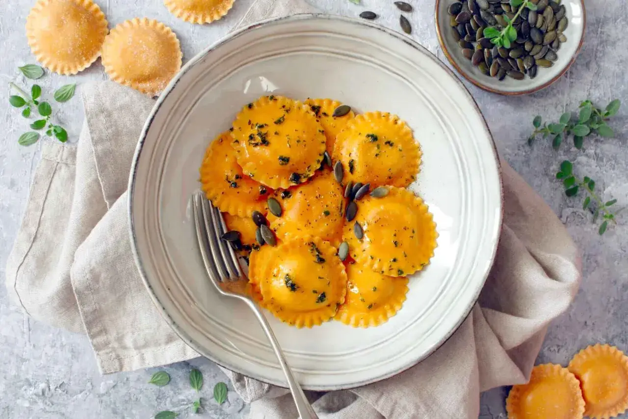 Un piatto invitante di tortelli di zucca, conditi con erbe e semi di zucca, pronti per essere gustati.