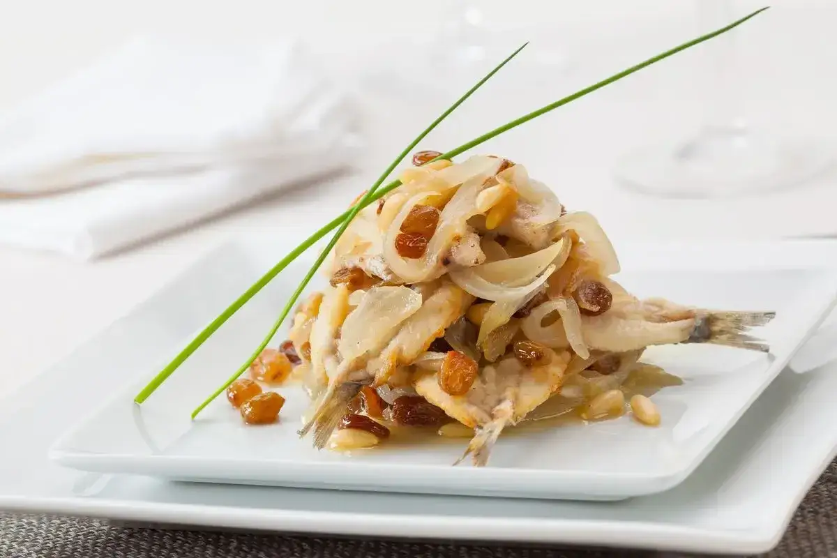 Sarde in saor, un classico veneto: sarde fritte con cipolle caramellate, uvetta e pinoli, guarnite con erba cipollina.
