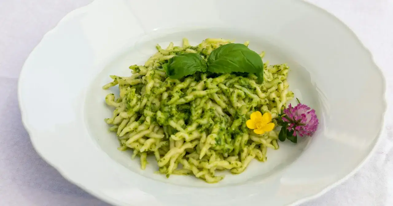 Un piatto di pasta con pesto fresco, guarnito con foglie di basilico e fiori di campo.