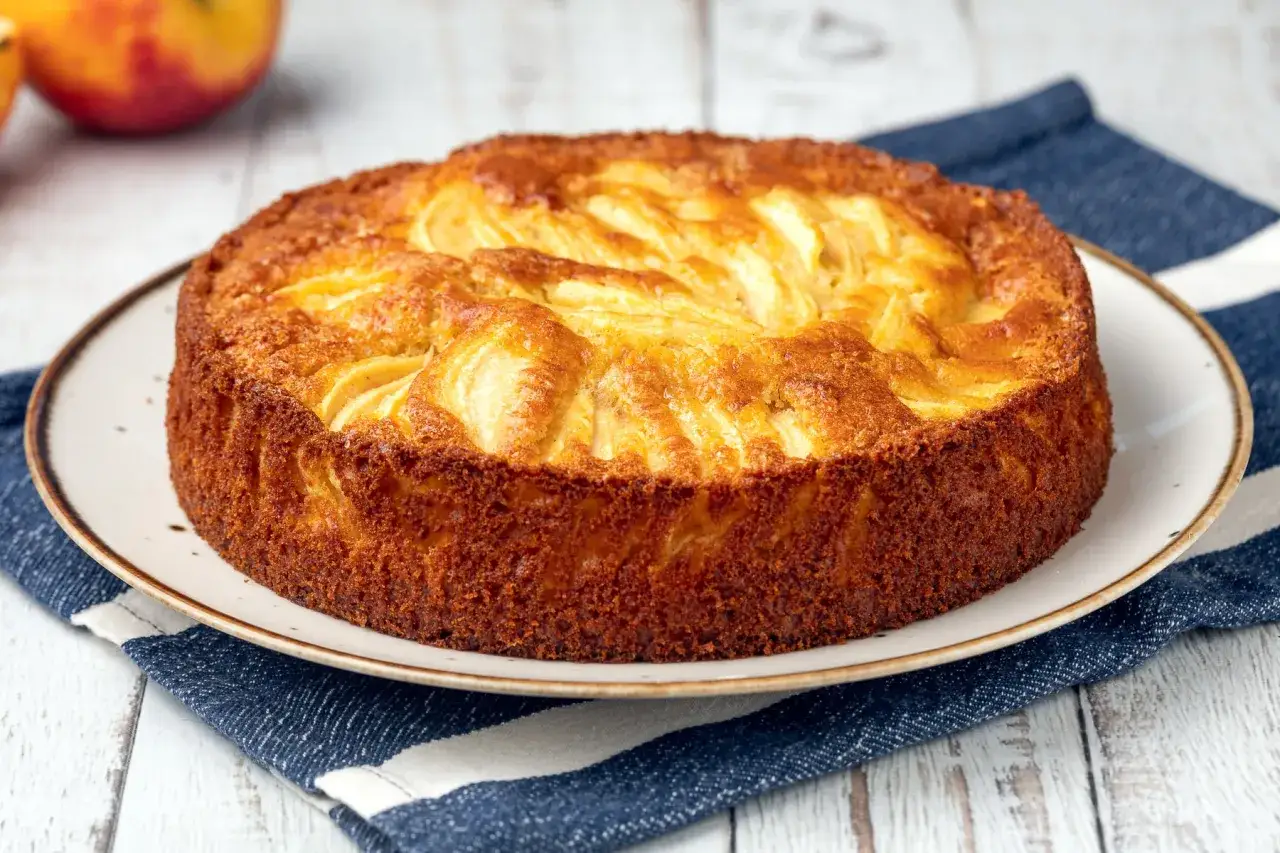 Torta di mele senza burro dorata e invitante, con mele a vista sulla superficie, servita su un piatto con tovagliolo a righe.