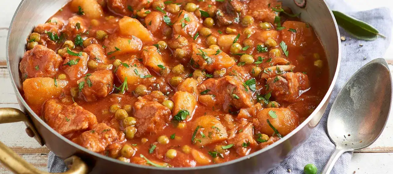 Un saporito spezzatino con piselli e patate, cotto in un sugo rosso e guarnito con prezzemolo fresco.