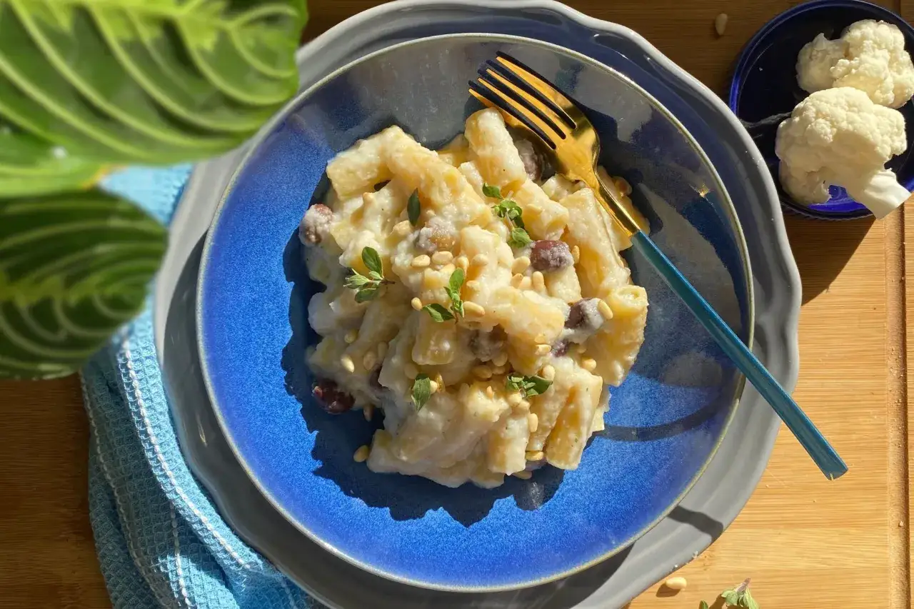 Piatto di pasta e cavolfiore cremoso, guarnito con pinoli e erbe aromatiche. Un primo piatto invitante e gustoso.