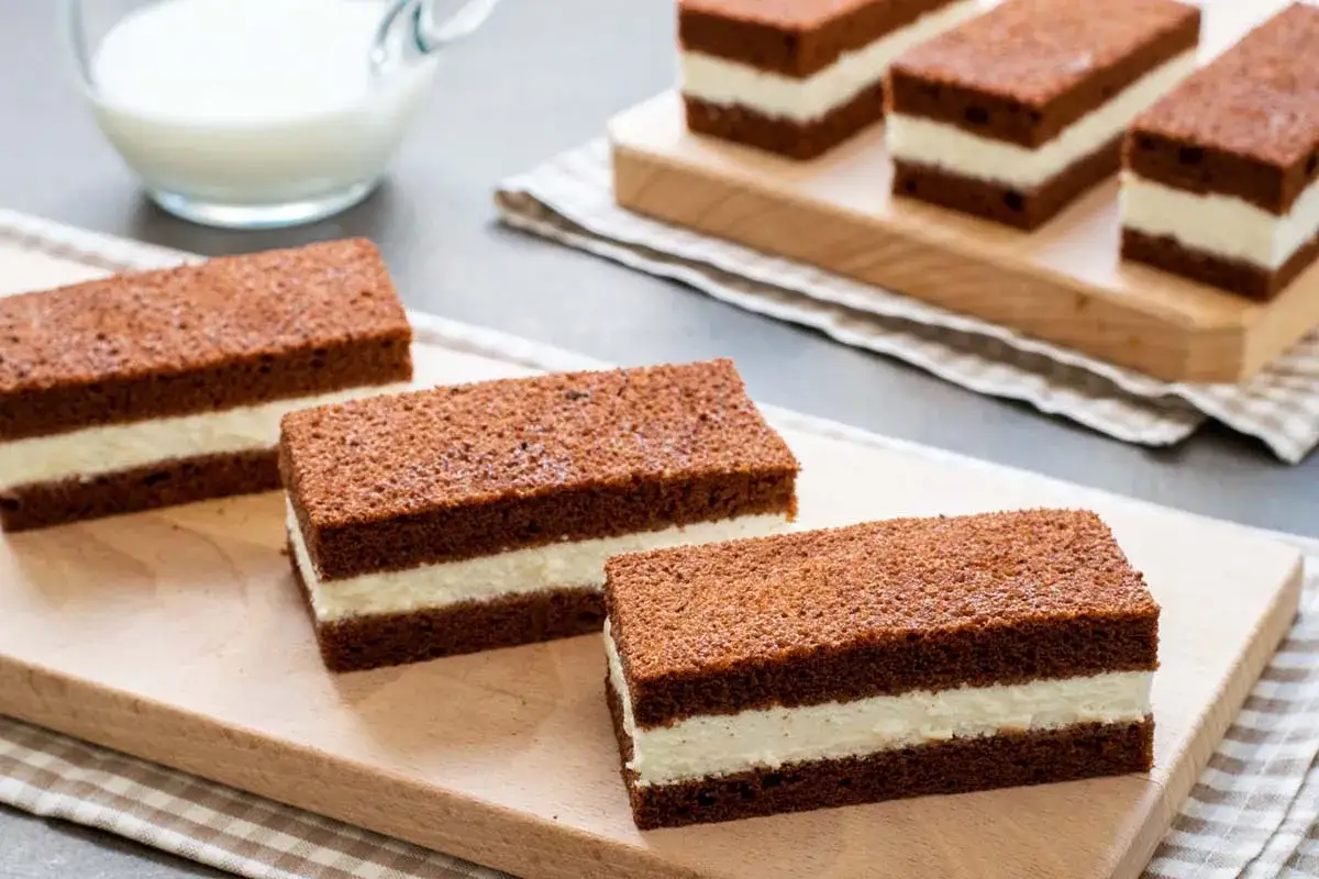 Fette al latte, soffici e golose, con strati di pan di Spagna al cacao e crema bianca. Perfette per una pausa dolce.