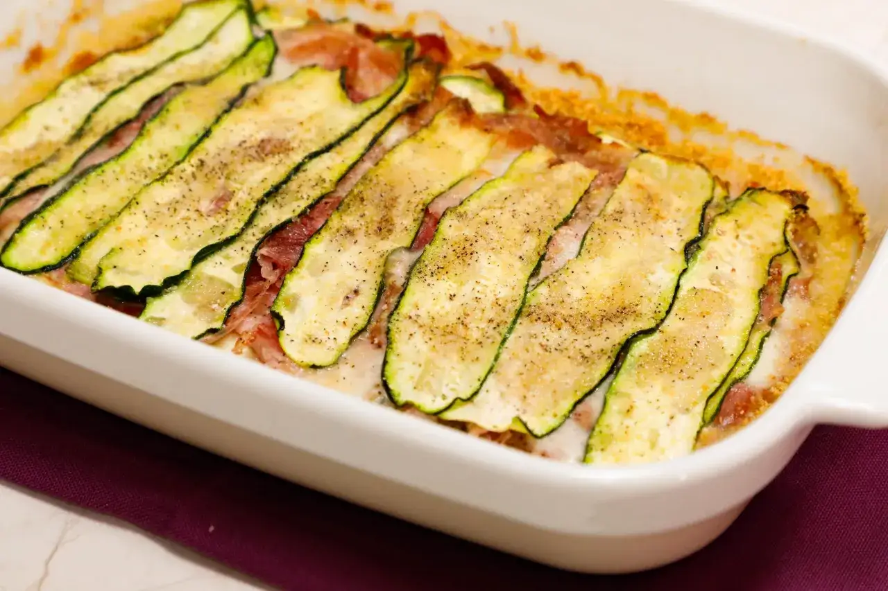 Sformato di zucchine appena sfornato, con fette sottili di zucchina grigliata, prosciutto e formaggio filante, condito con pepe nero.