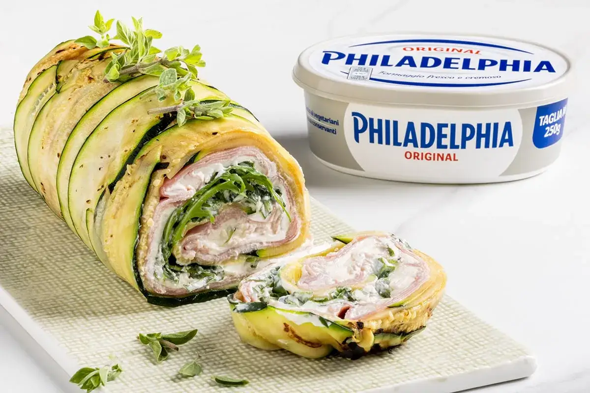 Rotolo di zucchine ripieno di prosciutto e formaggio cremoso Philadelphia, guarnito con erbe aromatiche.