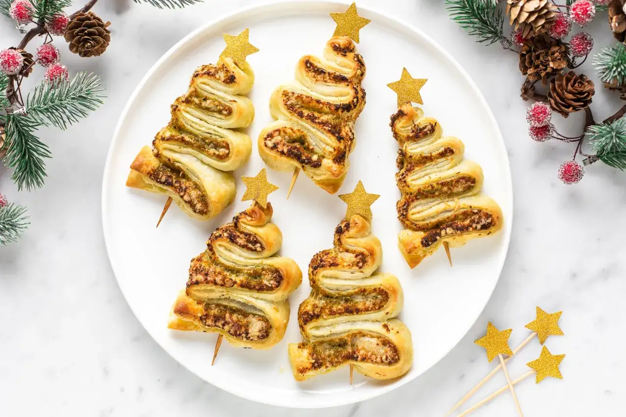 Alberi di sfoglia ripieni, perfetti antipasti di Natale, decorati con stelle dorate e rami natalizi.