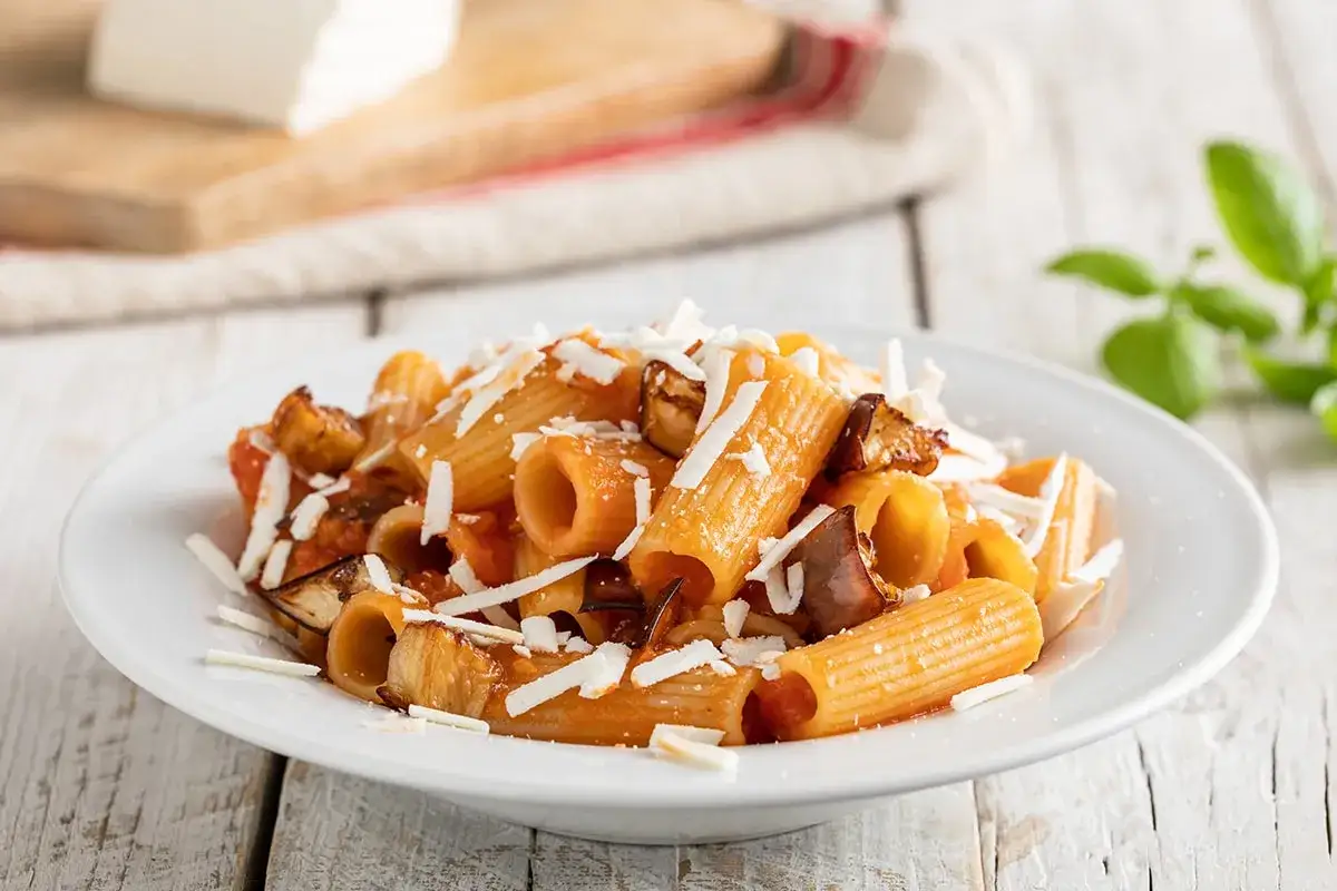 Un piatto invitante di pasta alla norma con melanzane fritte, pomodoro e ricotta salata grattugiata.
