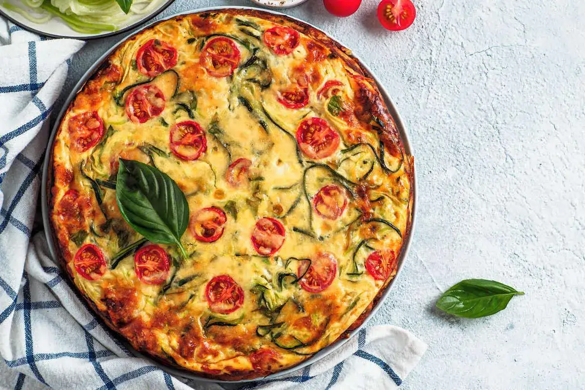 Torta salata vegana con zucchine e pomodorini, guarnita con basilico fresco.