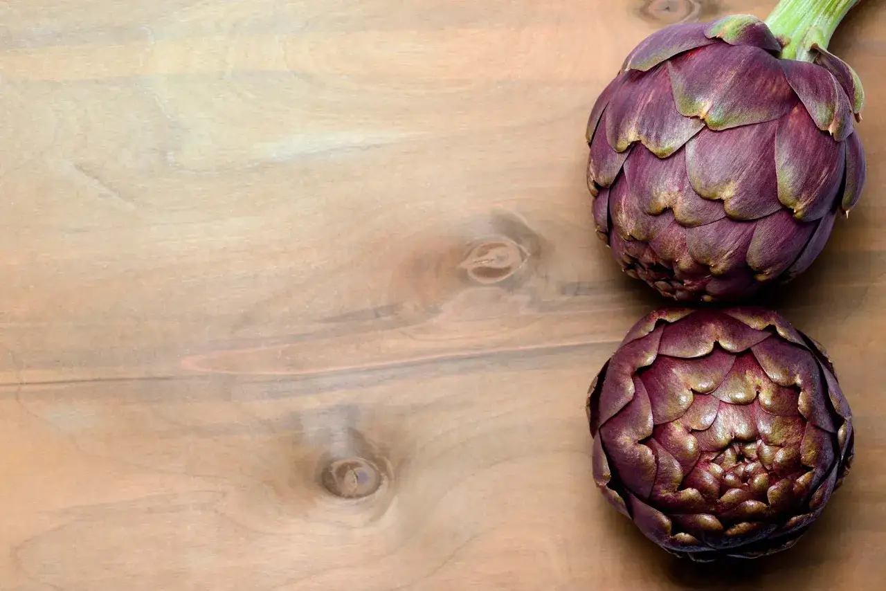 Due carciofi viola su un tavolo di legno, pronti per scoprire come cucinare i carciofi.