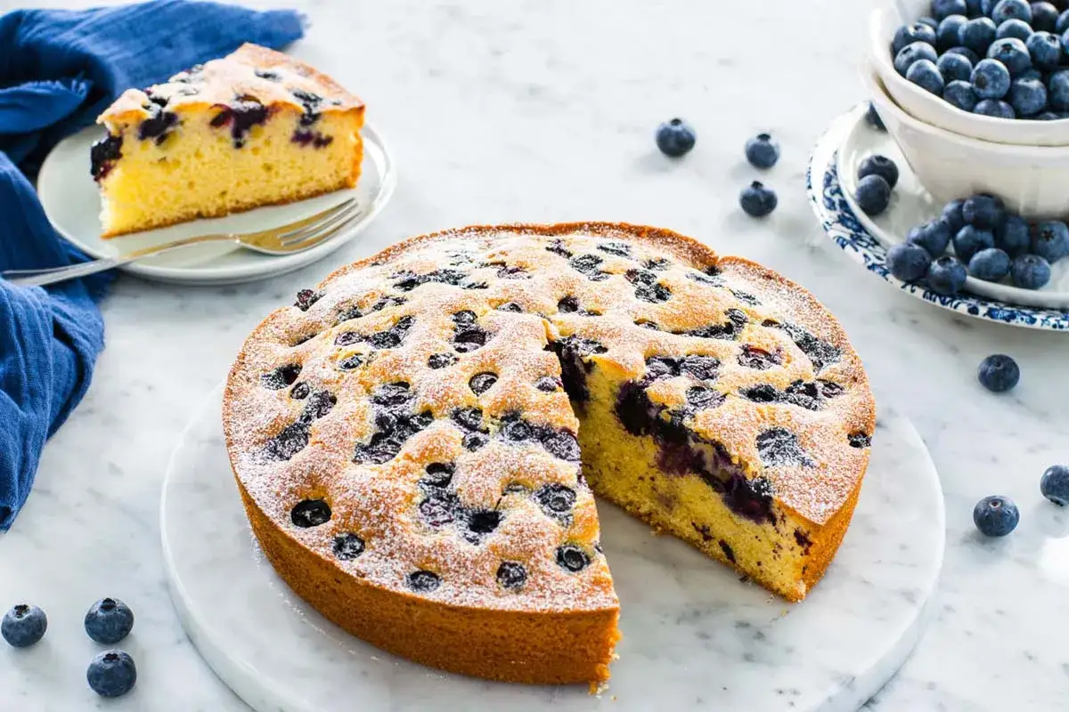 Una deliziosa torta 7 vasetti ai mirtilli, cosparsa di zucchero a velo, con una fetta gi&agrave; servita.
