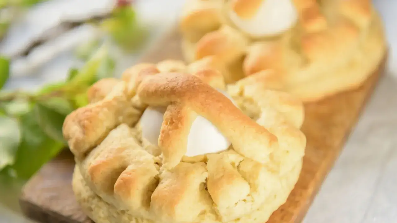 Dolci pasquali pugliesi con uovo intero, decorati con pasta intrecciata, su tagliere di legno.