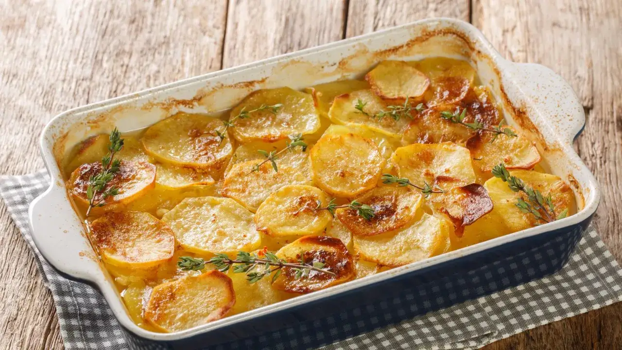 Parmigiana di patate dorata e profumata al timo, servita in una teglia blu su un tavolo di legno rustico.