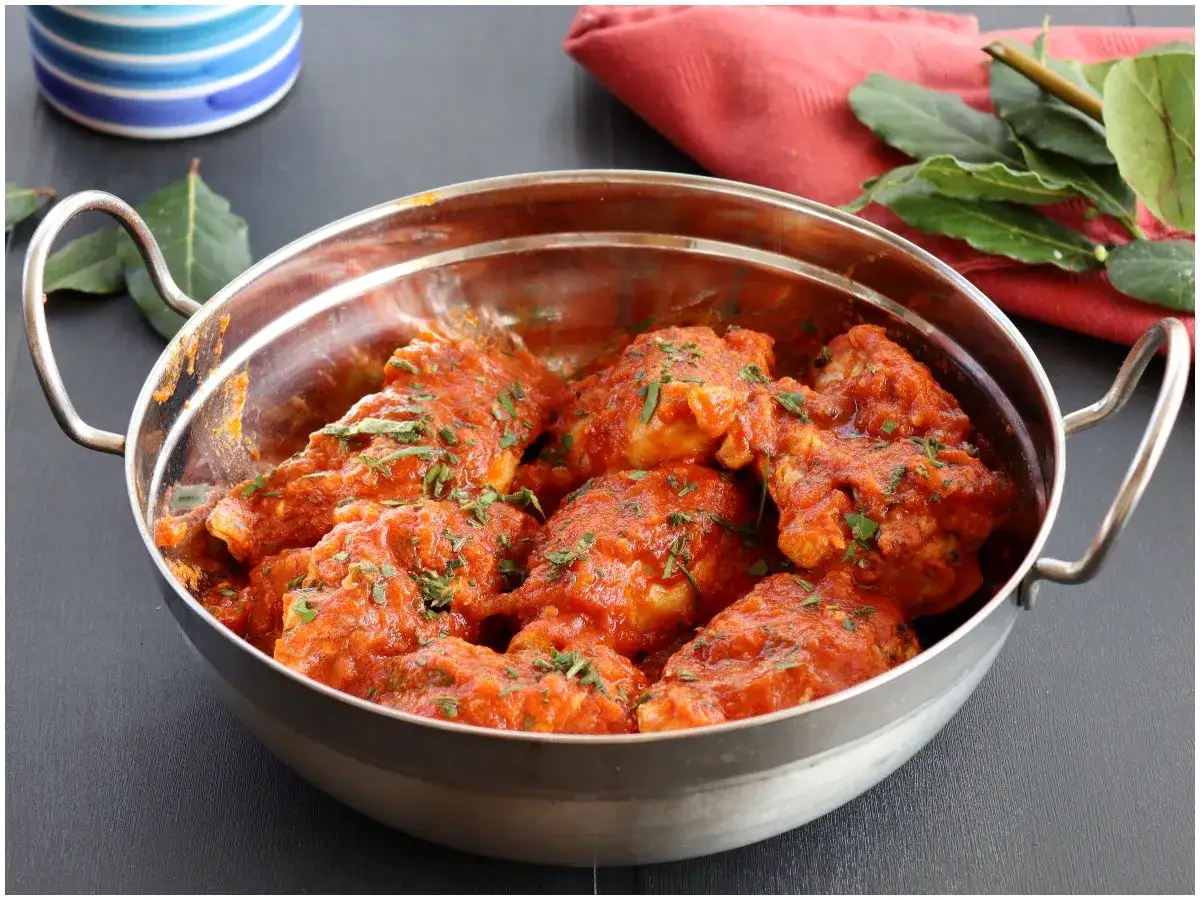 Un saporito coniglio in umido, cotto lentamente in una ricca salsa rossa e guarnito con erbe fresche, servito in una ciotola metallica.