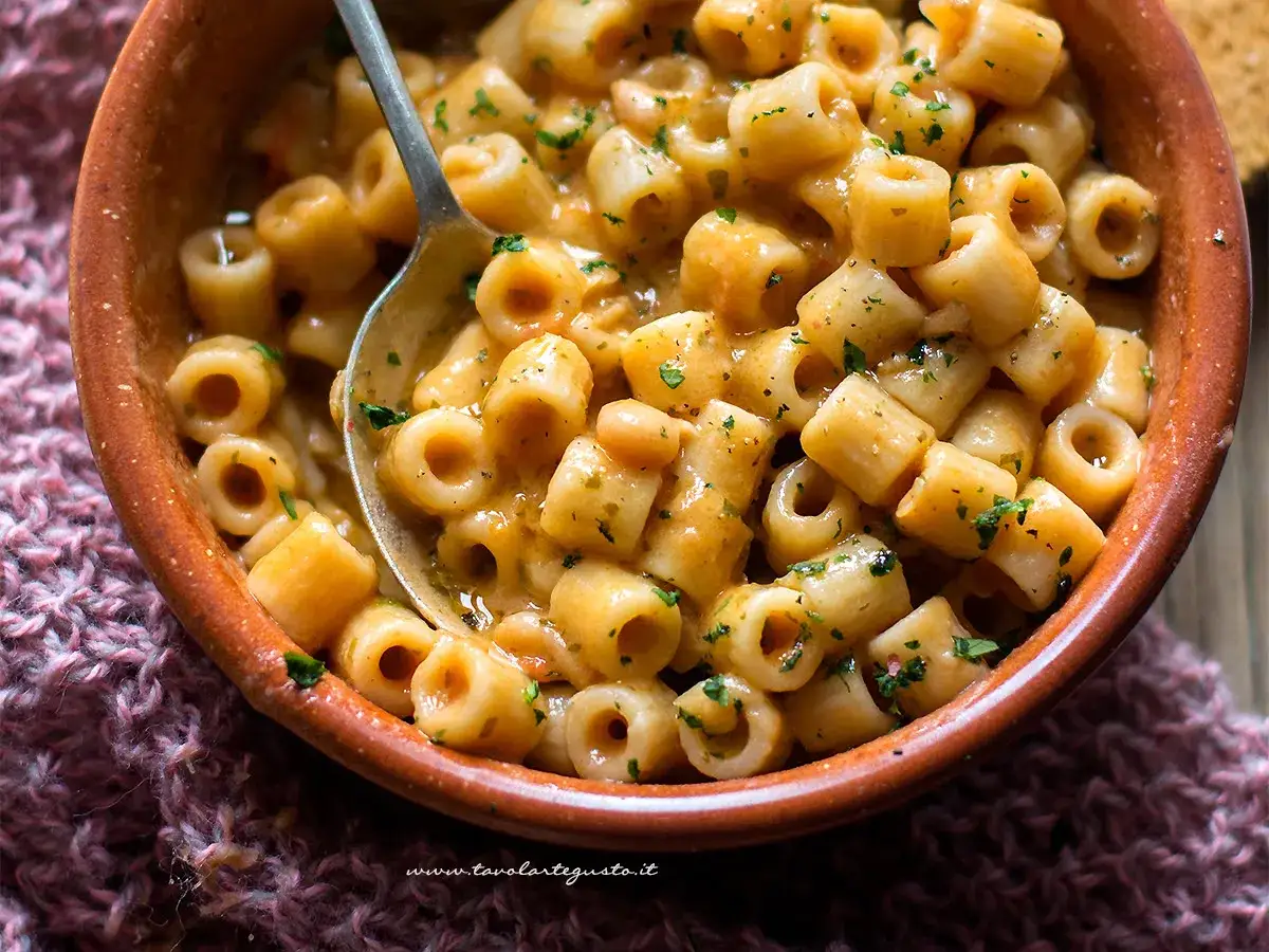 Un piatto fumante di pasta e fagioli in scatola, condita con prezzemolo fresco, servita in una ciotola di terracotta.