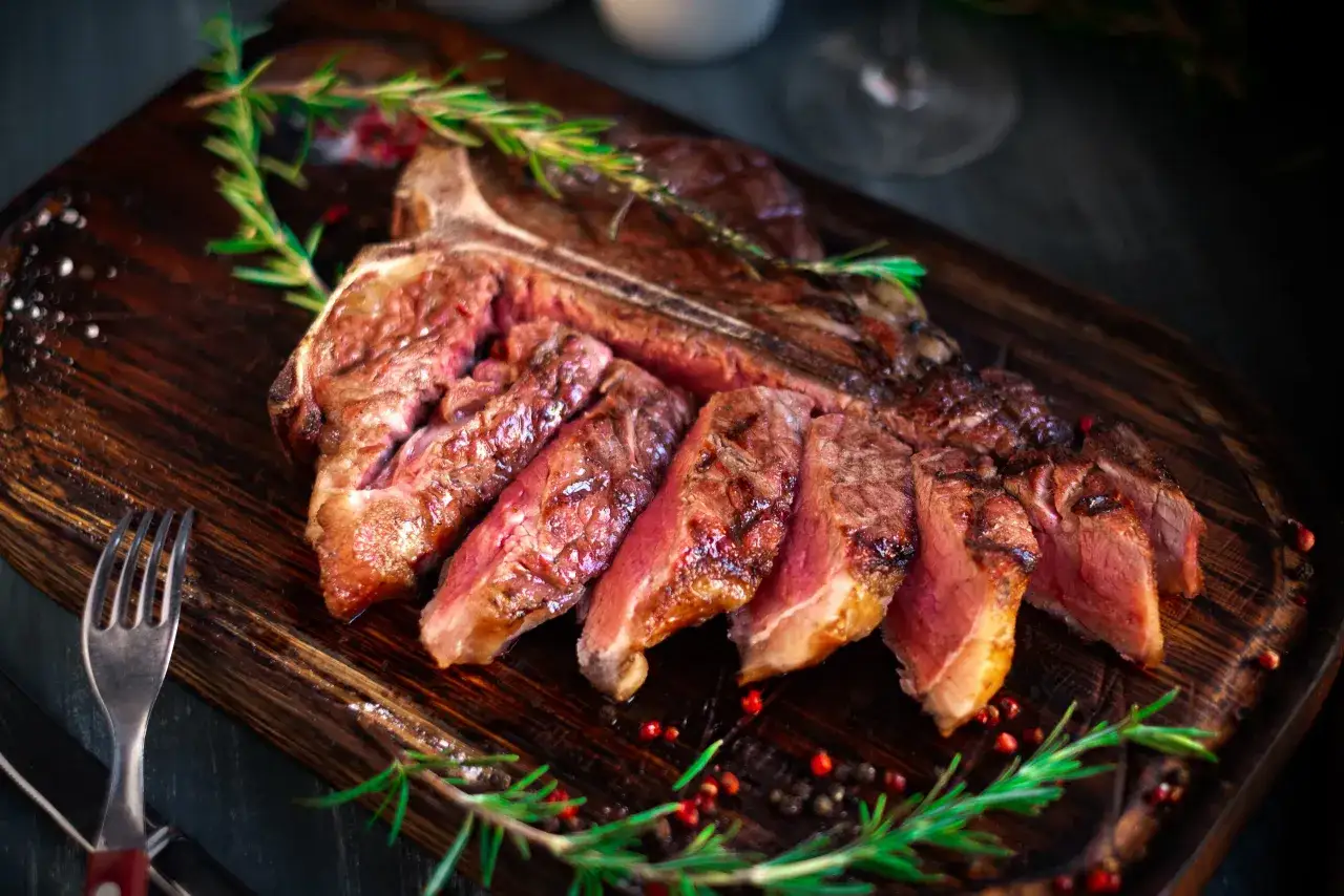 Succulenta costata di manzo affettata, guarnita con rosmarino e pepe rosa su tagliere di legno scuro.