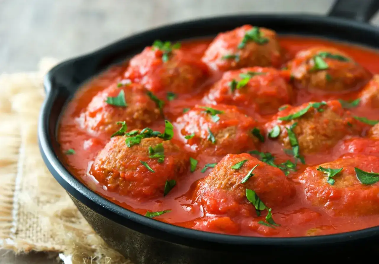 Polpette di carne succulente in salsa di pomodoro, guarnite con prezzemolo fresco, servite in una padella di ghisa.