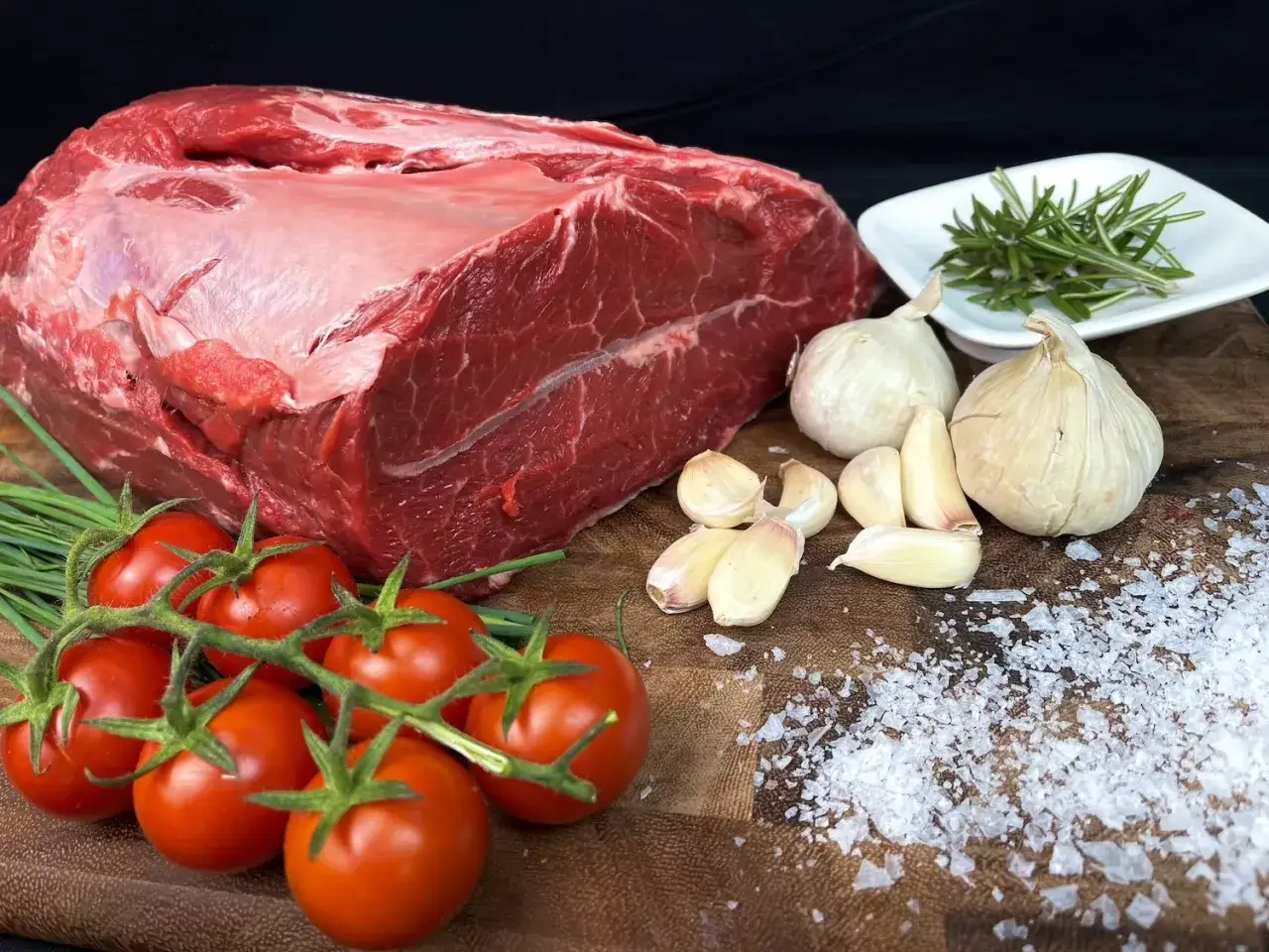 Un succulento arrosto di manzo pronto per essere cucinato, con pomodorini, aglio, rosmarino e sale grosso.