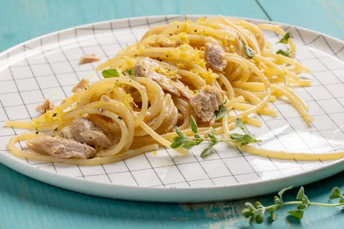 Un piatto di pasta tonno e limone, condita con scorza di limone grattugiata e erbe aromatiche fresche, servita su un piatto a scacchi.
