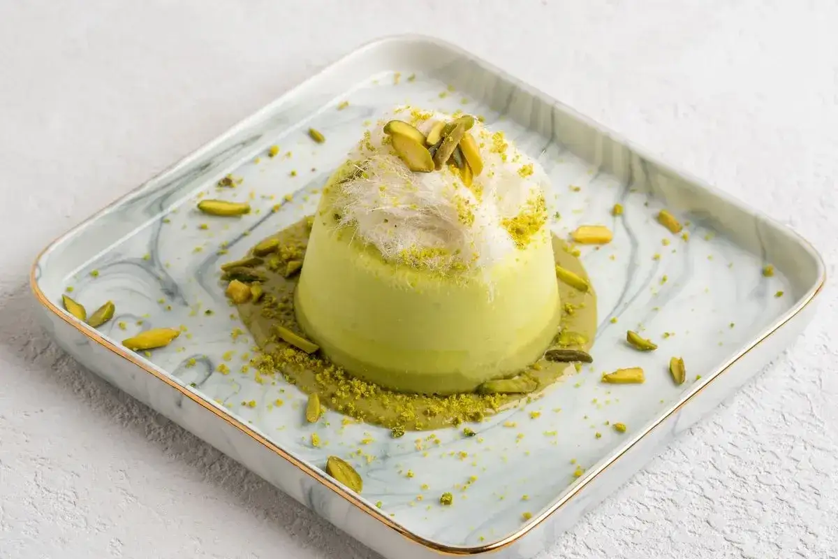 Delizioso semifreddo al pistacchio, guarnito con fili di zucchero filato e pistacchi tritati, servito su un piatto di marmo.